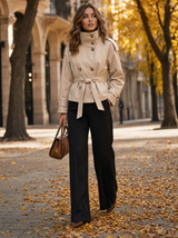 Vrouw in korte beige trenchcoat met ceintuur op een herfstallee