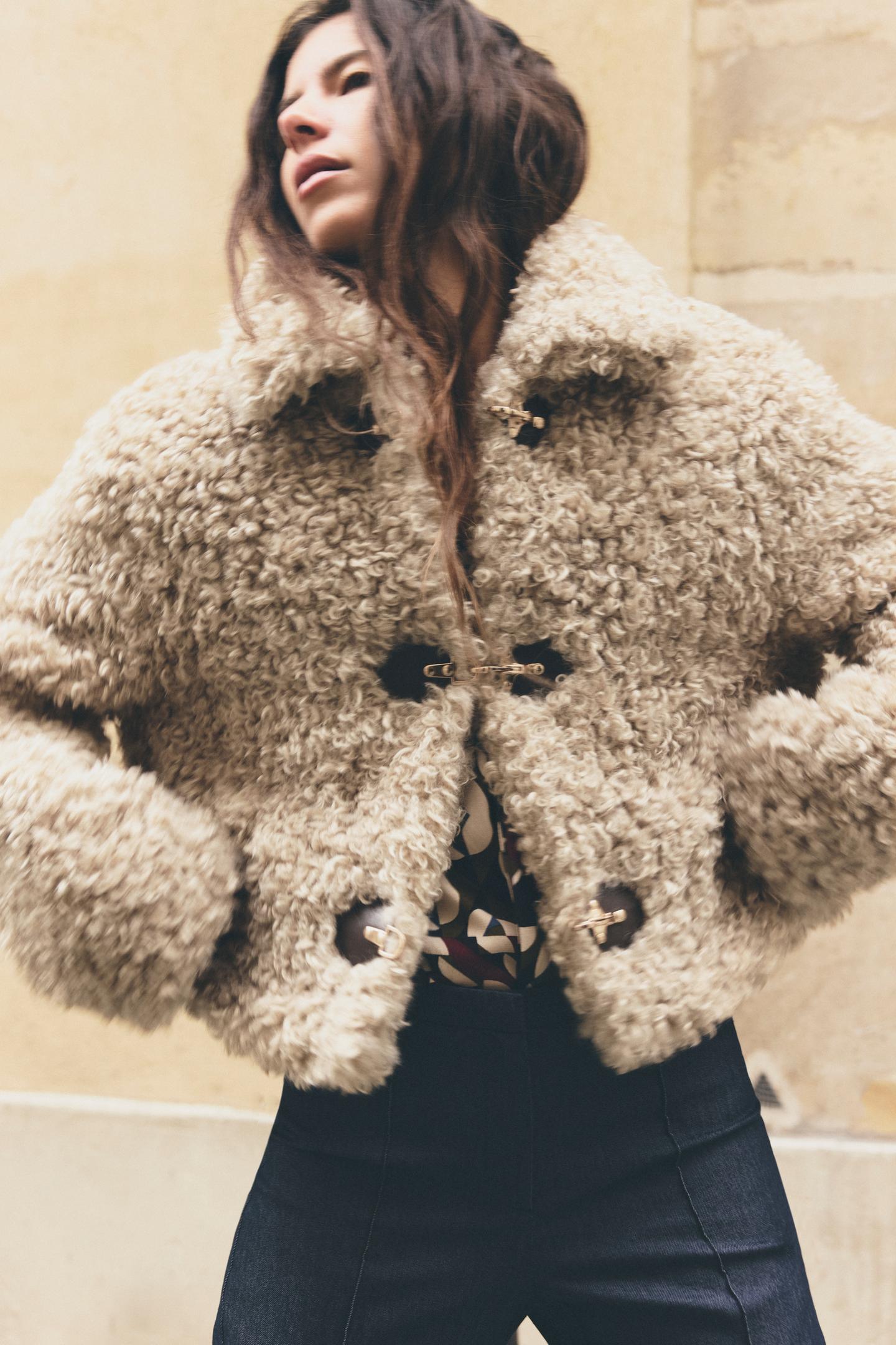 vrouw draagt beige teddy jas met gouden gespen en donkere jeans