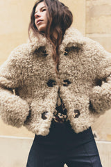 vrouw draagt beige teddy jas met gouden gespen en donkere jeans