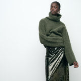 vrouw combineert groene gebreide coltrui met sequin rok