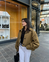 vrouw draagt camel cropped trench jacket met zwarte top en witte broek