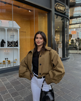 vrouw draagt camel cropped trench jacket met zwarte top en witte broek