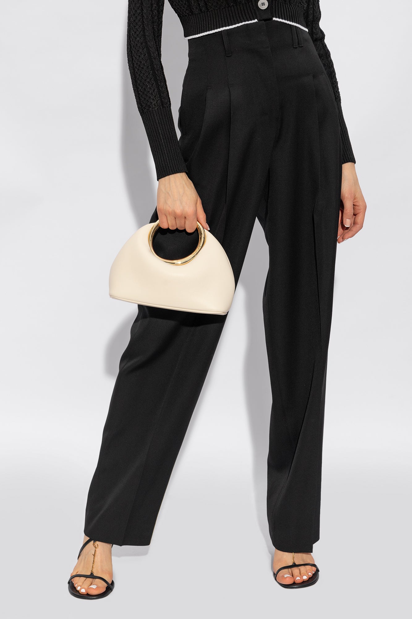 ivoren ring-handle handtas met gouden handgreep gestyled met zwarte pantalon en sandalen