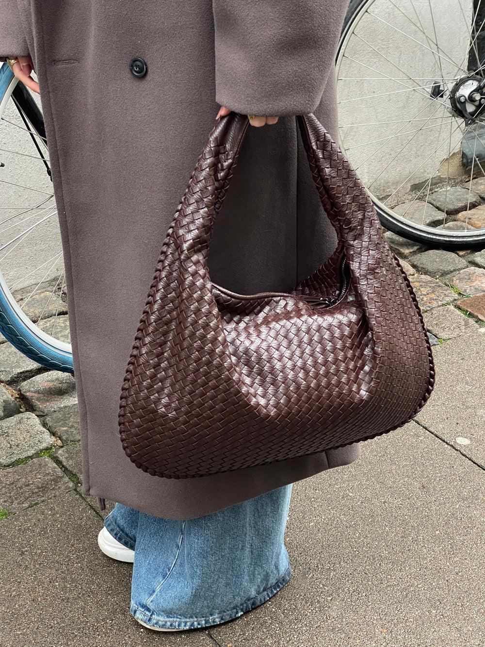donkerbruine gevlochten schoudertas gedragen door vrouw met lange jas