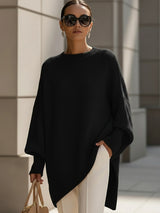 Zwarte oversized trui met ronde ribhals en gedropte schouders, gedragen met een witte pantalon en beige tas