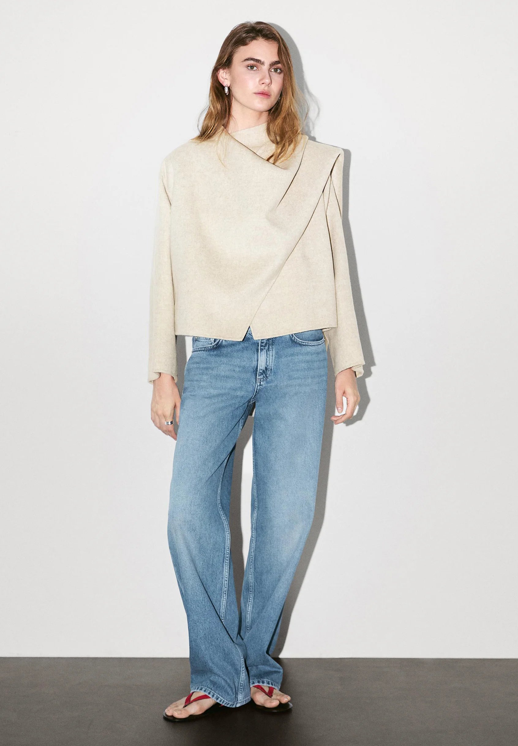 model draagt beige asymmetrische jas met sjaaldetail en jeans