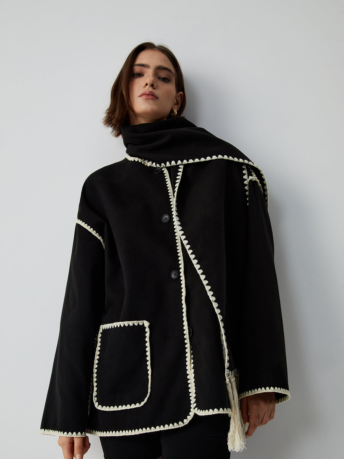 zwarte wikkel cape-jas met crème bies en franjes, close-up vooraanzicht op model