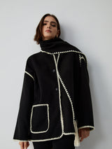 zwarte wikkel cape-jas met crème bies en franjes, close-up vooraanzicht op model