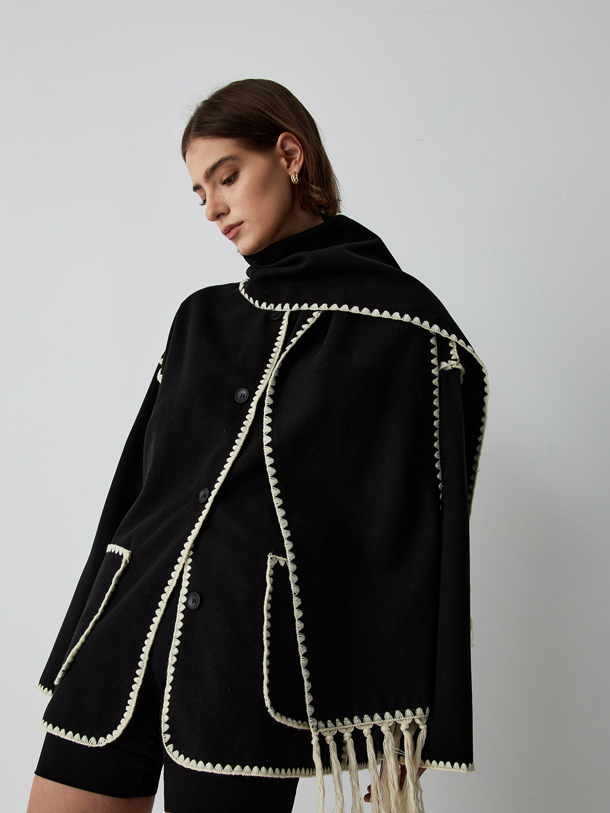 zwarte cape-jas met geïntegreerde sjaal en contrasterende bies, gedragen door model