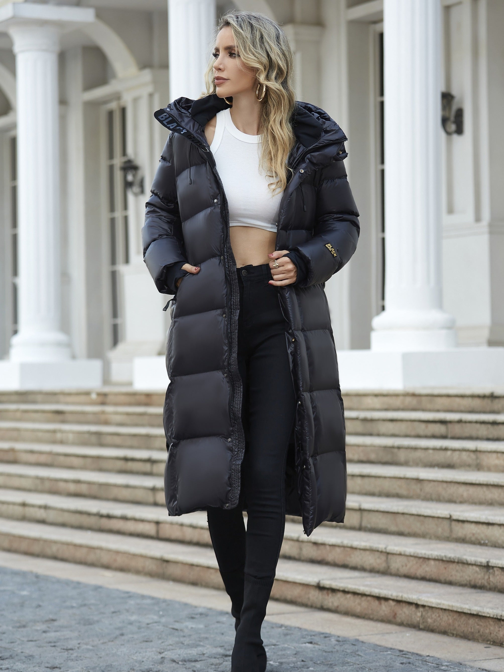 model draagt lange zwarte puffer jas met capuchon en laarzen, full body shot