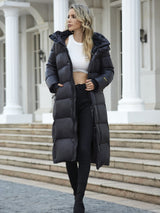 model draagt lange zwarte puffer jas met capuchon en laarzen, full body shot