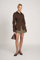 vooraanzicht van model met bruine Jaeda Wrap Shirt en geruite mini-rok