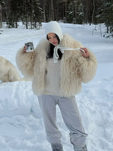 vrouw draagt beige fluffy jas in de sneeuw met witte broek en laarzen
