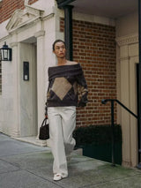 vrouw combineert off-shoulder bruine argyle trui met witte broek en handtas