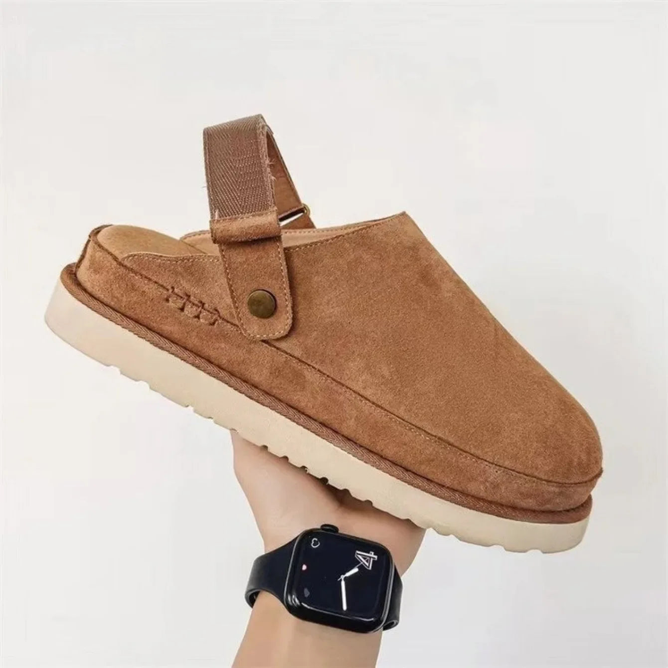 cognackleurige suède clogs met stevige zool en verstelbare band, hand houdt schoen vast