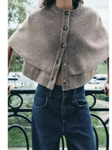 model draagt taupe gebreid vest met cape-look en knopen, gecombineerd met jeans