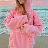 voorkant roze hoodie met quote en capuchon, gedragen op het strand