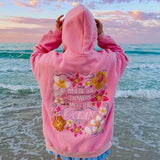 roze hoodie met geborduurde bloemen en tekst 'where the flowers meet the ocean' op het strand