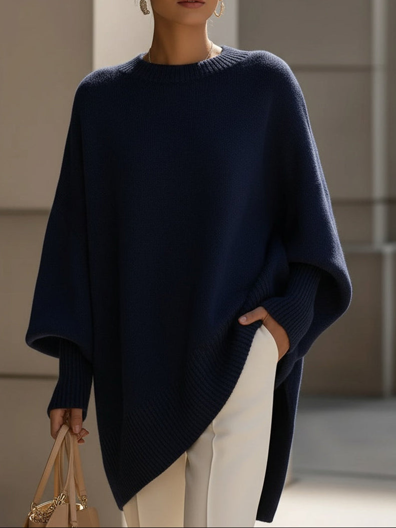 Marineblauwe oversized trui met vleermuismouwen en ribzoom, met de langere zijkant zichtbaar over een witte broek