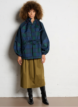 model met krullend haar in lange ruitregenjas en laarzen