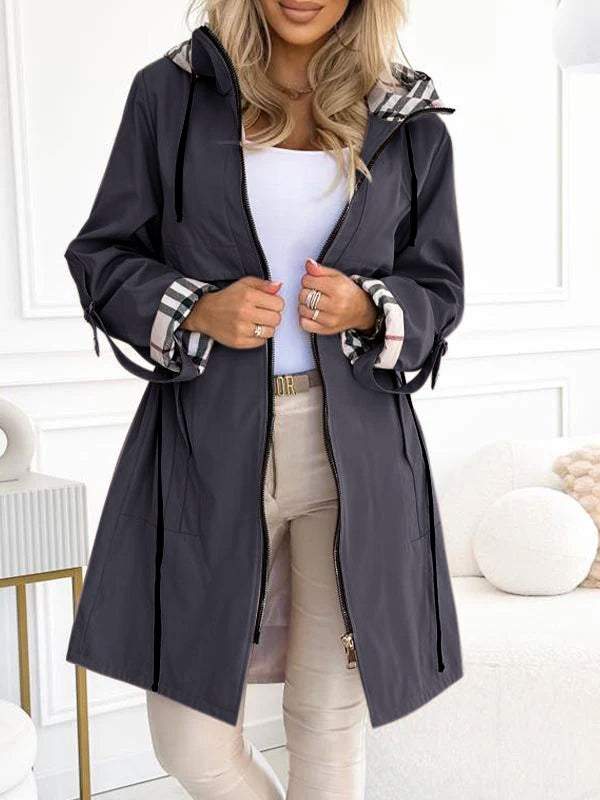 Donkergrijze trenchcoat met capuchon en ruitdetail, gedragen door vrouw.